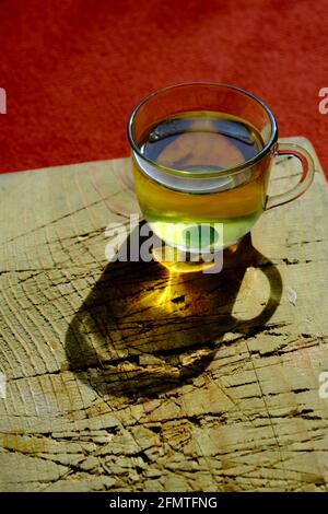 Tasse de thé de linden isolée en verre et il y a de la sueur et des bonbons vert mentholés. Pot en verre rempli de thé entièrement en linden existant sur une plaque en bois Banque D'Images