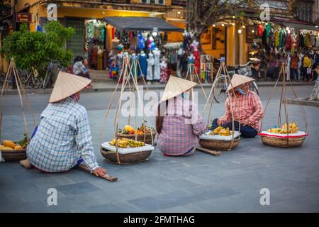 Les hustlers vietnamiens portant des paniers jumeaux et des bâtons d'épaule attendent que les touristes prêtent leurs marchandises pour des occasions photographiques, Hoi an, Vietnam Banque D'Images