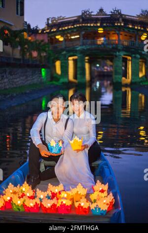 Couple vietnamien assis en bateau devant le pont japonais libérer des lanternes flottantes colorées dans la rivière, Hoi an, Vietnam Banque D'Images