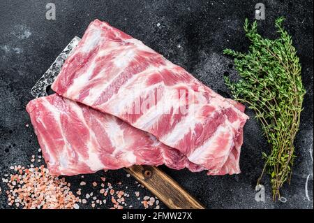Côtes de porc crues non cuites sur le couperet de viande de boucher. Arrière-plan noir. Vue de dessus Banque D'Images