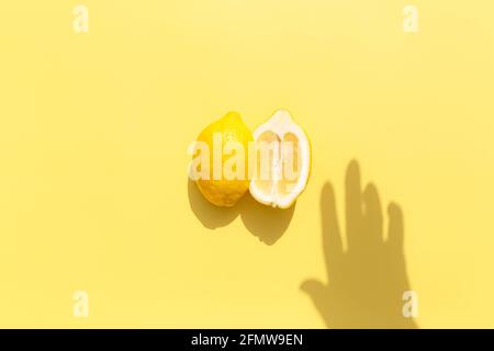 Deux demi-morceaux de citron avec ombre de la main sur fond jaune. Concept de saine alimentation, de voyage ou de vacances Banque D'Images