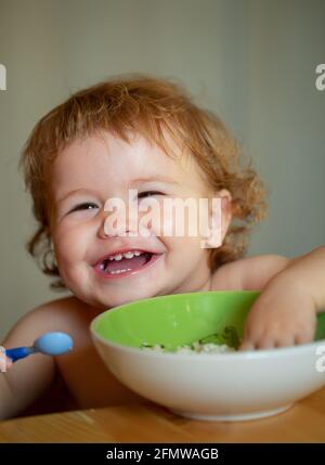 Bébé drôle manger de la nourriture lui-même avec une cuillère sur la cuisine. Bébé souriant mangeant de la nourriture. Banque D'Images