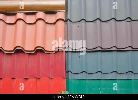 Une exposition de tuiles de toit en métal orange, rouge, gris, marron et vert, différents types de tuiles de toit en métal ondulé pour couvrir le toit de la maison. Banque D'Images