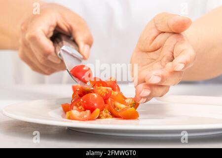 Mains déposant des tomates fraîchement coupées sur une assiette Banque D'Images