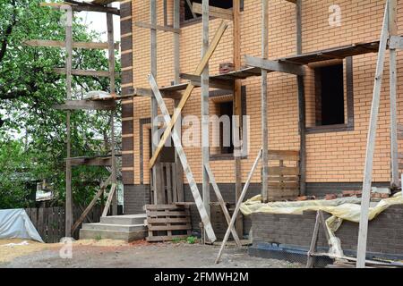 Vue sur une nouvelle maison en brique en construction avec échafaudage, fenêtres non installées et porche non fini. Nettoyer le chantier de construction. Banque D'Images