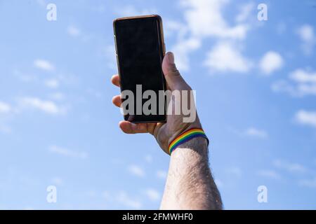 remettez le téléphone portable avec un bracelet de couleur lgtb avec le ciel en arrière-plan. Banque D'Images
