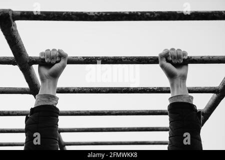 Bras d'un homme faisant des pull-ups à un lieu d'entraînement de rue post-soviétique, image de moody monochrome Banque D'Images