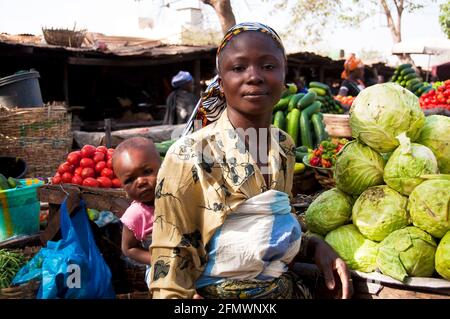 BAMAKO, MALI - VERS FÉVRIER 2012 : vendeuse de légumes transportant sa fille sur son dos dans l'un des marchés de Bamako. Banque D'Images