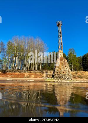 vieux phare en métal rouillé abandonné avec une grande fondation en pierre au bord de la mer avec un reflet dans l'eau. rive de falaises de grès. Pierres de rivage. Banque D'Images