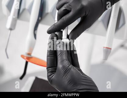Gros plan des mains du dentiste tenant la pièce à main dentaire en acier inoxydable. Stomatologue tenant un instrument mécanique pour les procédures dentaires. Concept de la dentisterie, de la stomatologie et des outils dentaires. Banque D'Images