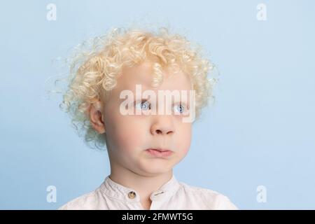 Gros plan mignon petit garçon d'âge préscolaire posant isolé sur fond bleu de studio. Banque D'Images