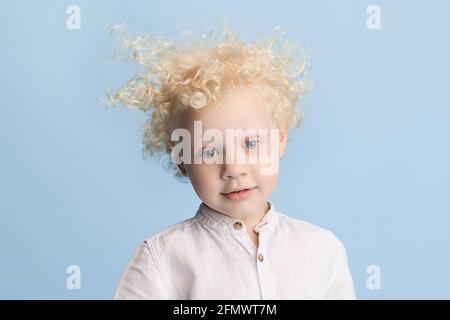 Gros plan mignon petit garçon d'âge préscolaire posant isolé sur fond bleu de studio. Banque D'Images