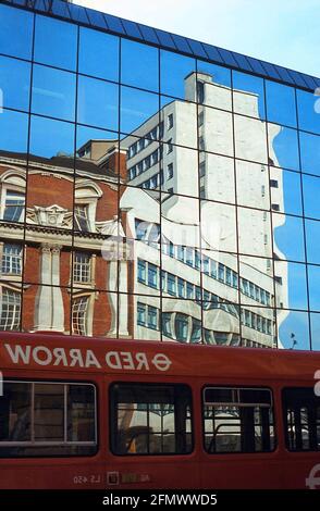 Réflexions sur un bâtiment à façade de verre avec un bus rouge au premier plan. Photo vintage de 1985 Banque D'Images