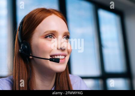 Gros plan d'une belle jeune femme opérateur utilisant un micro-casque lors de l'assistance à la clientèle au bureau à domicile. Banque D'Images