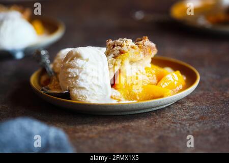 Biscuit fraîchement préparé, cobbler à la pêche servi avec de la glace à la vanille française sur un fond rustique sombre. Banque D'Images