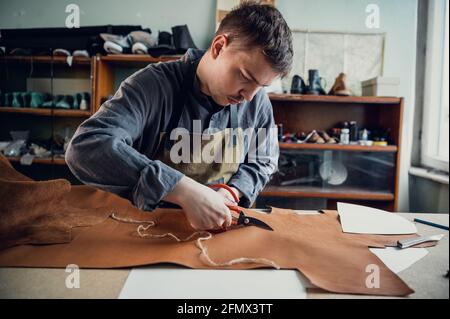 Lors de la masterclass pour la production de chaussures, un cordonnier expérimenté découpe du cuir avec des ciseaux. Banque D'Images
