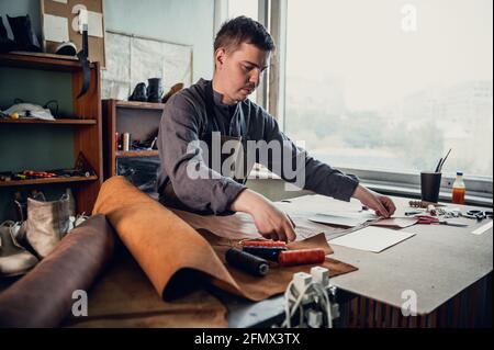 Un jeune cordonnier de la vieille école remplit un ordre de fabriquer un produit en cuir exclusif. Portrait en studio. Banque D'Images