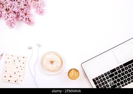 Ordinateur de bureau très féminin, clavier d'ordinateur portable, tasse de café et beignet, fleurs lilas. Composition de pose à plat, bloc-notes, Cappuccina, réduite au minimum Banque D'Images