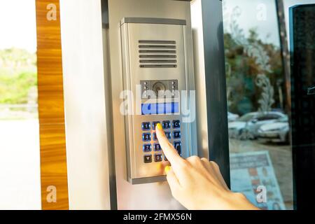 Gros plan de la main de la femme entrant le code du système de sécurité, en appuyant sur le bouton avec l'index sur l'interphone moderne avec écran lcd bleu près de l'entrée d Banque D'Images