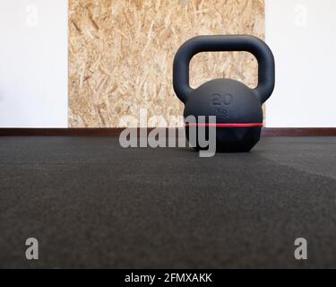 20kg kettlebell noir isolé sur le sol à la salle de gym. Équipement de musculation et de fitness avec panneau de protection mural en bois à l'arrière-plan Banque D'Images