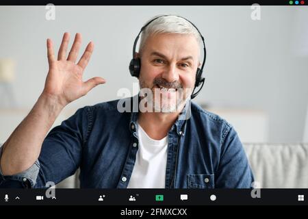 Homme senior souriant ayant un appel vidéo, à l'aide d'un casque Banque D'Images