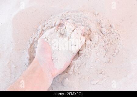 La main du gars prend ou touche le sable blanc de plage de près. Banque D'Images