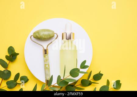 Flacon compte-gouttes en verre jaune à usage médical et cosmétique, rouleau de jade et branche d'eucalyptus sur fond jaune vif. Concept SPA. Vue de dessus, copie Banque D'Images