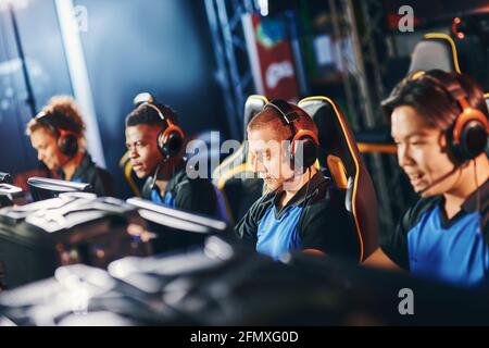 Équipe de quatre joueurs professionnels de cybersport portant des écouteurs participant au tournoi eSport, jouant à des jeux vidéo en ligne Banque D'Images