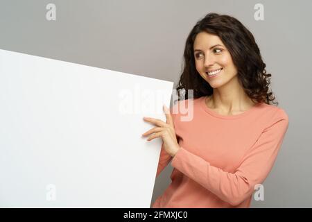 Les jeunes femmes tiennent le panneau d'affichage vide regarder de côté avec le sourire heureux pour copier l'espace à un écriteau vierge isolé Banque D'Images