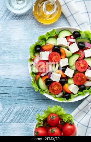 Salade de légumes grecs avec tomates cerises, concombres, fromage feta, olives et assaisonnées d'huile. Serviette blanche à carreaux sur une table en bois bleu. Haut v Banque D'Images