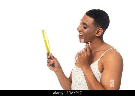 homme transsexuel afro-américain souriant tout en tenant le rouge à lèvres et le miroir isolé sur blanc Banque D'Images