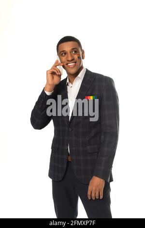 homme d'affaires afro-américain souriant avec drapeau lgbt peint sur le visage parler sur un smartphone isolé sur blanc Banque D'Images