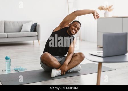 Joyeux Black Guy qui s'étire à l'ordinateur portable faire de l'exercice à la maison Banque D'Images