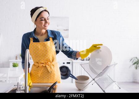 Bonne femme dans un tablier mettant une plaque sur un support dans la cuisine Banque D'Images