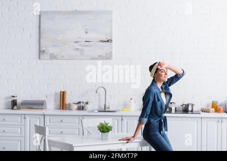 Femme de ménage dans une chemise en denim debout avec les yeux fermés près de la table Banque D'Images