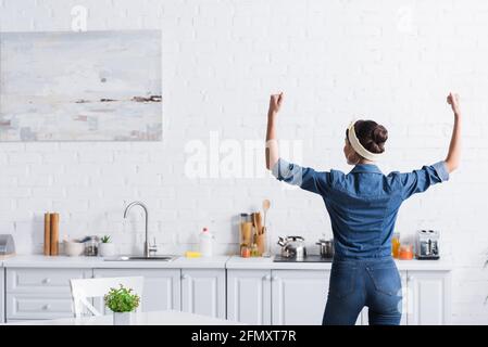 Vue arrière de la femme de ménage dans une chemise en denim montrant les muscles dedans cuisine Banque D'Images