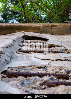 Vieux mur en béton écriteux avec un renfort en fer exposé et rouillé - la vue à angle bas révèle un feuillage dense qui dépasse le dessus du mur. Banque D'Images