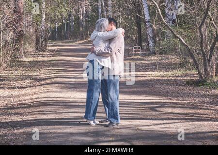 Couple interracial de personnes âgées dans des vêtements décontractés se embrassant dans un parc forestier de printemps. Une femme embrassant un homme sur la joue. Banque D'Images