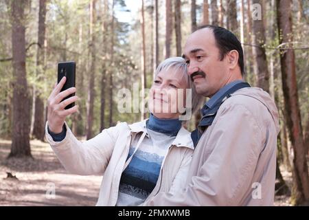 Couple interracial âgé vêque dans un parc forestier de printemps, en prenant un selfie sur votre téléphone Banque D'Images