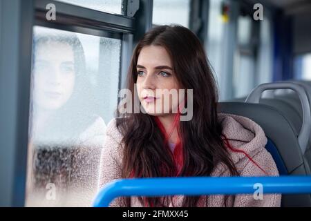 Une femme voyageant dans un bus et regardant à l'extérieur une fenêtre imbibée de pluie Banque D'Images
