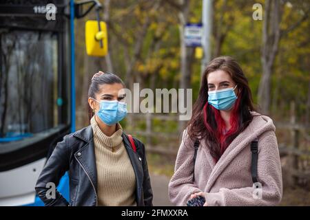 deux jeunes femmes portant des revêtements de visage et attendant devant un bus à un arrêt de bus. Banque D'Images