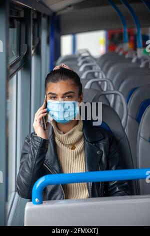 Femme voyageant dans un bus portant un masque facial et parlant sur un téléphone portable. Banque D'Images