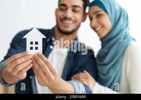 Jeune couple musulman tenant une maison de papier et souriant Banque D'Images