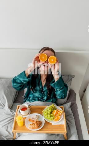 La jeune femme rit et tient les oranges près de ses yeux. Concept de bien-être et zone de confort à la maison. Banque D'Images