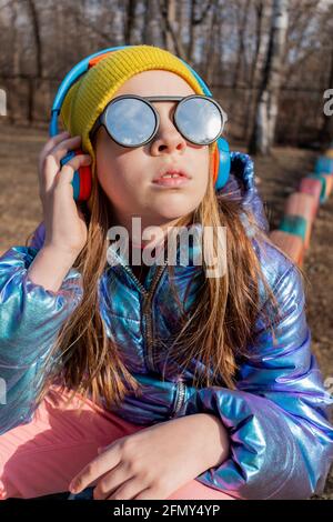 Une adolescente s'assoit à l'extérieur et écoute de la musique sur un casque. Concept bien-être et utiliser la technologie par enfant Banque D'Images