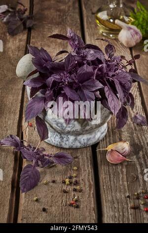 Basilic violet dans mortier de pierre avec condiments sur table en bois Banque D'Images