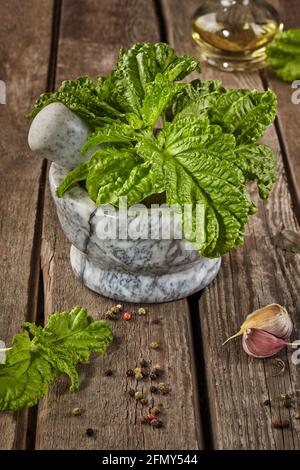 Mortier à pierre avec basilic et condiments sur table en bois Banque D'Images