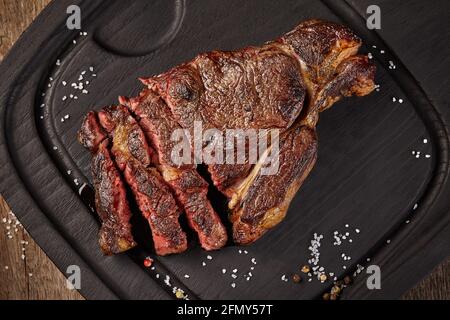 Steak de veau grillé en tranches avec condiments sur une planche de bois Banque D'Images