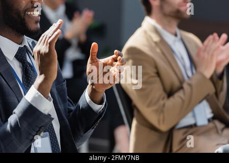 vue rognée d'un homme d'affaires afro-américain souriant applaudissant pendant le séminaire des collègues presque flous Banque D'Images