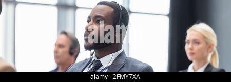 Homme d'affaires afro-américain dans un casque près de collègues flous, bannière Banque D'Images